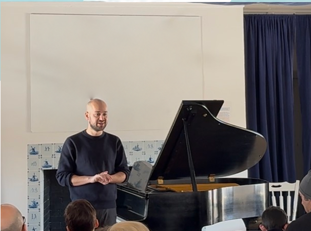 Yonathan Peled standing beside a grand piano while presenting at a student recital